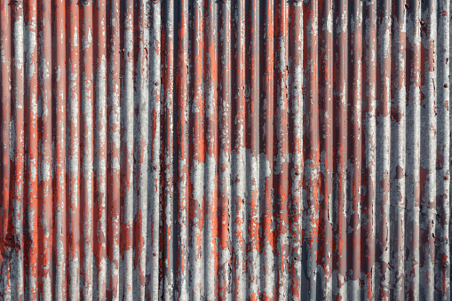 Red paint cracking and peeling on an old corrugated metal surface.