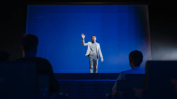 istock Successful Speaker Stands on Stage and Does New Product Presentation. Presenter / Motivational Speaker Greets Audience in Conference Hall, Starts His Entrepreneurship Presentation / Talk / Live Event 1226991358