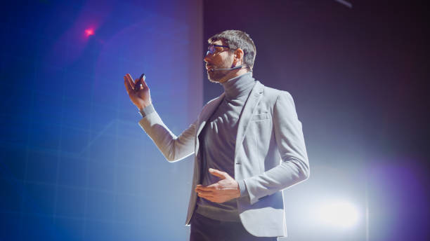istock On-Stage Handsome Speaker, Talks about His Ideas, Concepts and New Age Product, in Background Screen Animation. Live Entrepreneurship Event / Start-up Conference / Device Presentation 1226991383