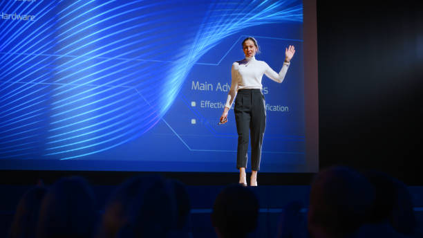 istock On-Stage Successful Female Speaker Presents Technological Product, Uses Remote Control for Presentation, Showing Infographics, Statistics Animation on Big Screen. Live Event / Business Conference 1226991407