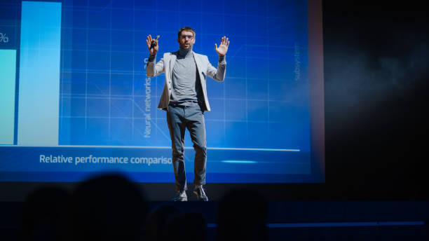 successful male speaker stands on stage, greets audience and presentation of the new product, shows infographics, statistics animation on screen. live event / device release / start-up conference - self improvement audio imagens e fotografias de stock