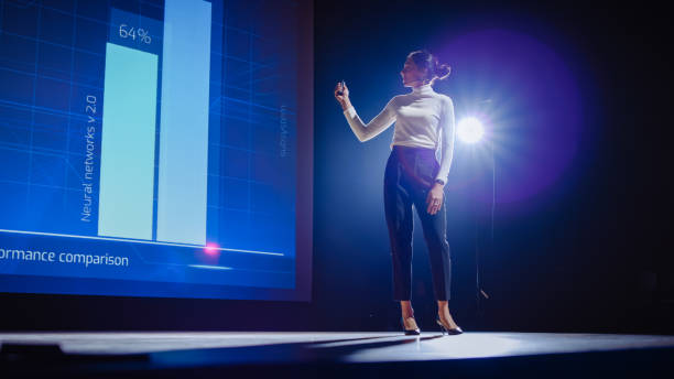 istock On-Stage Successful Female Speaker Presents Technological Product, Uses Remote Control for Presentation, Showing Infographics, Statistics Animation on Big Screen. Live Event / Business Conference 1226991449