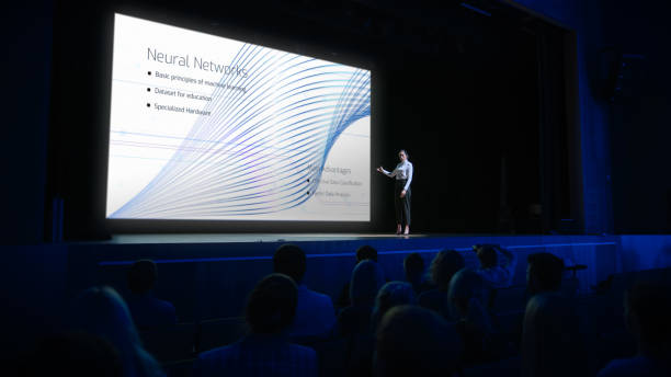 istock Computer Science Startup Conference: On Stage Speaker Does Presentation of New Product, Talks about Neural Networks, Shows New AI, Big Data and Machine Learning App on Big Screen. Live Event 1226991512