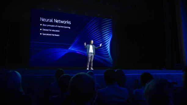 istock Startup Conference Stage: Speaker Presents New Product, Talks about Performance, Neural Networks, Artificial Intelligence, Big Data and Machine Learning. Live Business Event with Large Audience 1226991541