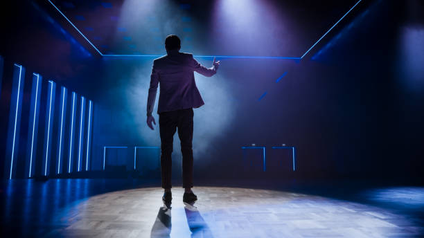 istock Famous Entertainer Stands on Stage, Greets Audience, Starts Performance. Software Company Founder, Tech Marketing Guru Making a Pitch, Presentation Speaker Giving Talk. Cinematographic Back View 1226991552