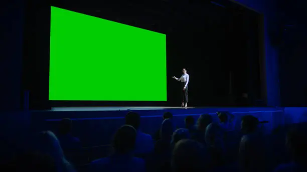 Photo of Inspirational Speaker Does Presentation New Product to Audience, Behind Her Movie Theater with Green Screen, Mock-up, Chroma Key. Female CEO Shows Leadership on Business Live Event or Device Reveal
