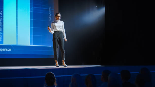 istock Tech Conference Stage: Visionary Female Speaker Talks about Product. Neural Networks, Artificial Intelligence, Big Data and Machine Learning. Infographics On Big Screen. Live Startup Business Event 1226991640