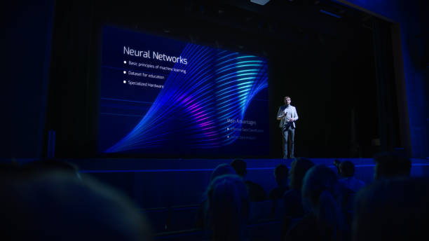 istock Computer Science Startup Conference: On Stage Speaker Does Presentation of New Product, Talks about Neural Networks, Shows New AI, Big Data and Machine Learning App on Big Screen. Live Event 1226991664