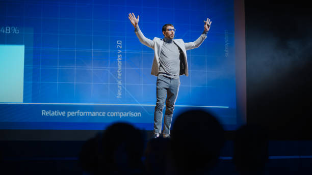 istock Successful Male Speaker Gets on Stage, Greets Audience and Does Presentation of the Technological Product, Shows Infographics, Statistics Animation on Screen. Live Event / Start-up Conference 1226991710