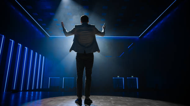 istock Famous Entertainer Gets on the Stage, Greets Audience, Starts Performance. Software Company Founder, Tech Marketing Guru Making a Pitch, Presentation Speaker Giving Talk. Cinematographic Back View 1226991817