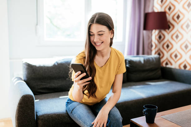 istock Happy young woman sitting on couch at home and using phone during quarantine 1226991998