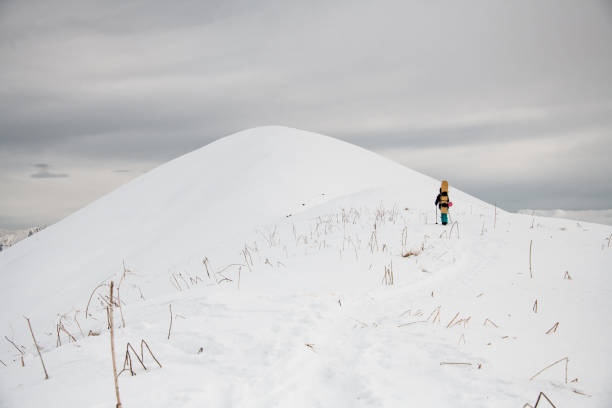 istock man with snowboard on his back climbs along path to snowy mountain. 1226997720