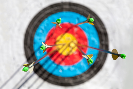 One out of six arrows in the bull's-eye of an archery target. Selective focus with the focus being on the back end of the arrow, with an out of focus target.