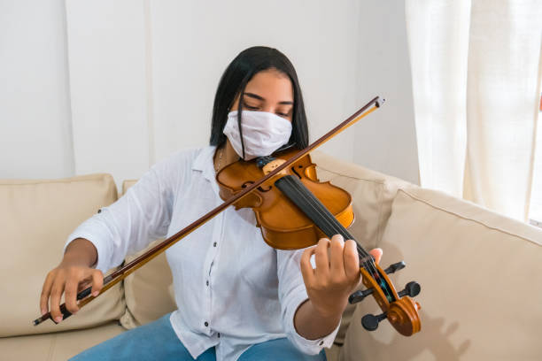 schöne und niedliche frau mit einer gesichtsmaske spielen die geige zu hause - practicing music violin women stock-fotos und bilder