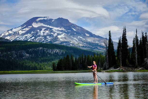 young woman paddle boards across lake - women paddleboard bikini surfing imagens e fotografias de stock