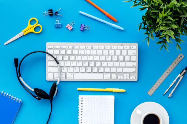 istock E-learning. Stationery, headphones and keyboard on blue table top-down frame 1227005328