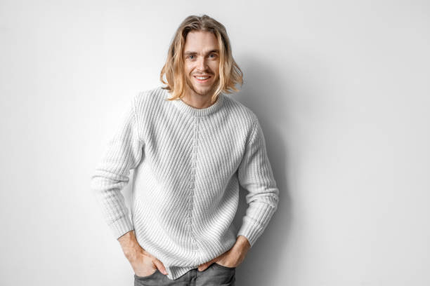 istock Freestyle. Young man in sweater standing isolated on white posing to camera hands in pockets joyful 1227005532