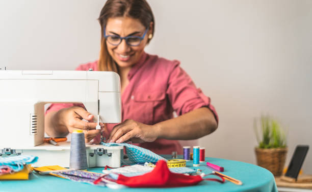 happy latin tailor seamstress woman sewing with machine homemade medical face mask for preventing and stop corona virus spreading - textile industry and covid19 healthcare concept - seam needle textile industry thread imagens e fotografias de stock