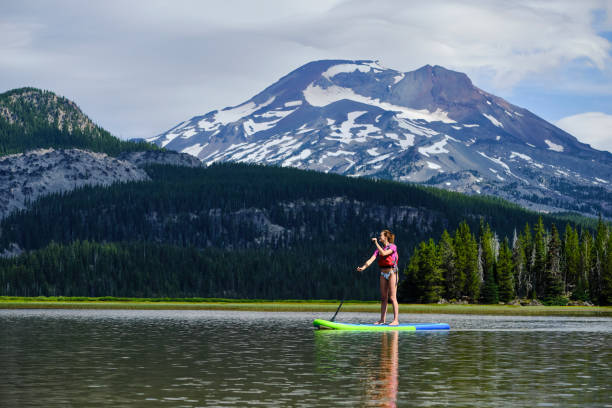 Young woman paddle boards across lake