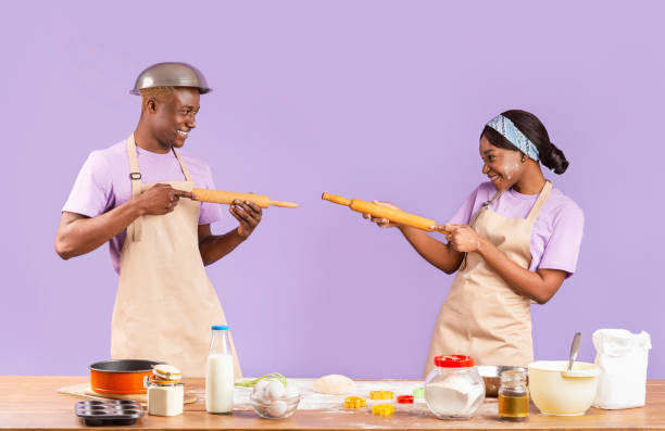 istock Black girl and guy having fun fighting with rolling pins while baking on violet background 1227008770