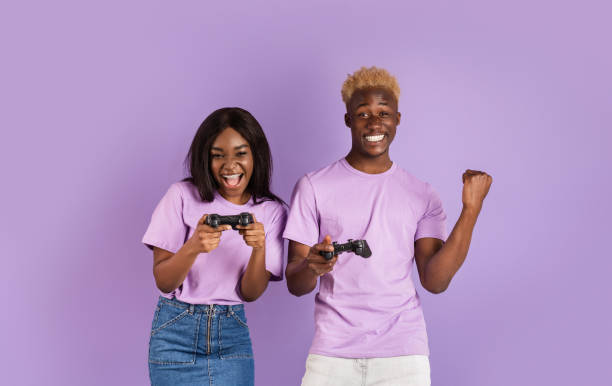 istock Fun hobbies. Cool black guy playing video games with his girlfriend on lilac background. Panorama 1227008781
