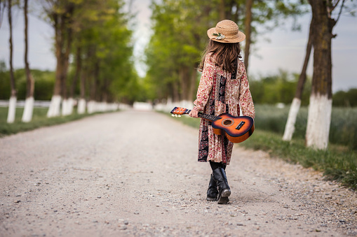 Child walking down the road with ukulele guitar in her hand