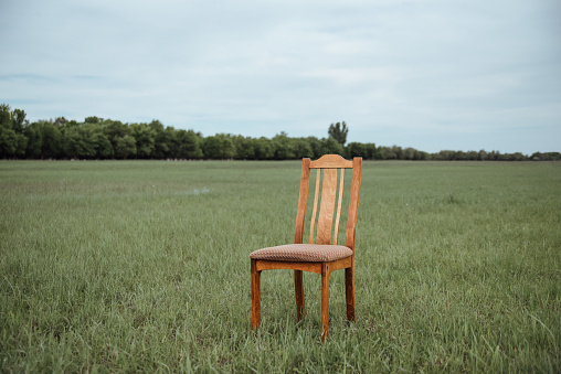 A wooden chair stands in the middle of a field.A chair in the middle of the field. The concept of loneliness and emptiness. Depression