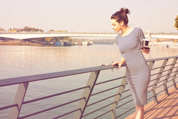 Cute trendy woman drinking coffee/tea and using cellphone on the river.