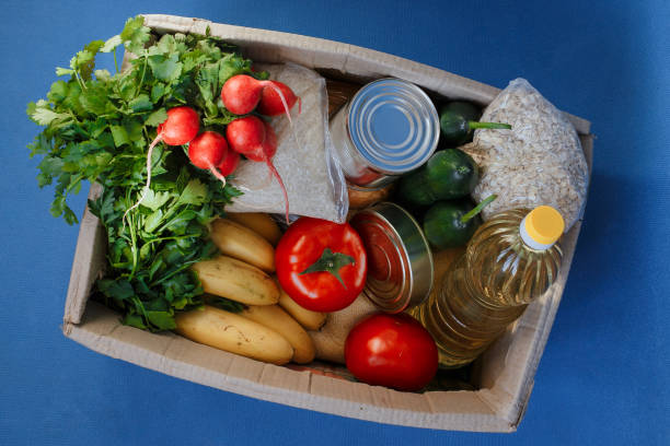 Donation box with food. Donation box with food on a blue background. Fruits, vegetables, canned food, pasta and sunflower oil in a box. Social assistance with food. food bank stock pictures, royalty-free photos & images