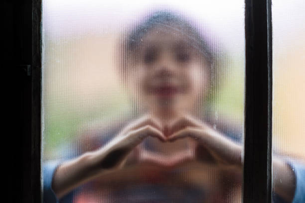 Isolated boy making heart symbol through window glass