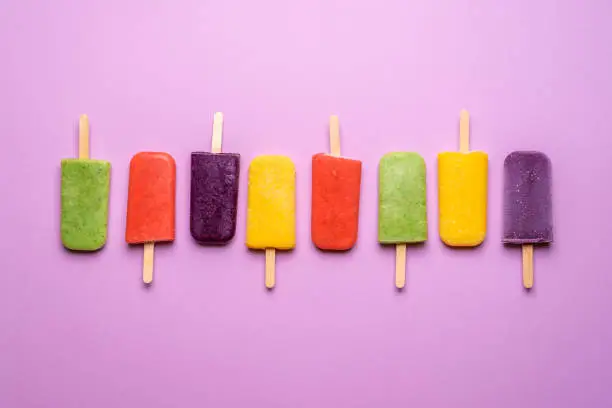 Ice cream popsicles diversity lined up on a purple background. Flat lay of multi-flavored ice creams on sticks. Refreshing vegan dessert.