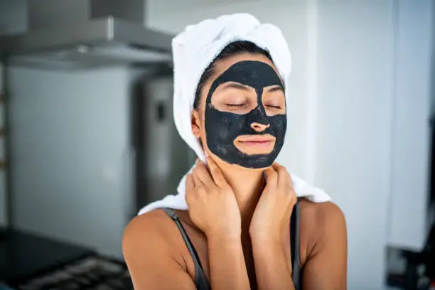 Portrait of a smiling Latin woman using beauty treatment at home . She have black facial mask and she has her eyes closed