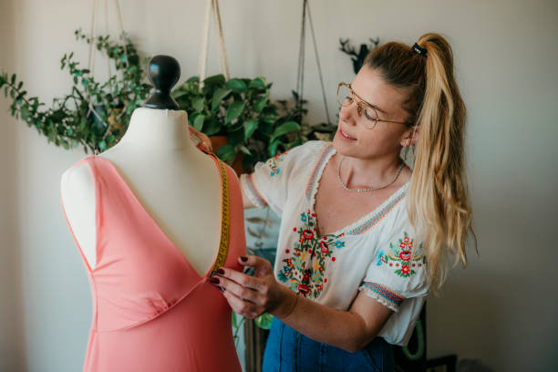 マネキンを測定する若い女性のファッションデザイナー、居心地の良い家や仕立屋でダミーで作業するテープを保持している縫い目、洋裁や縫製のコンセプト、 - owner embroidery small business indoors ストックフォトと画像