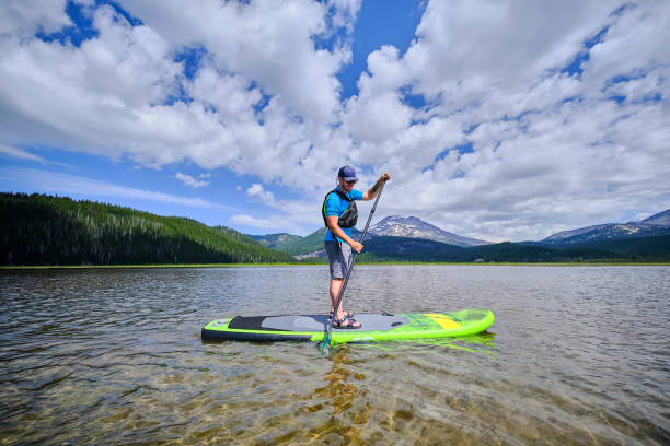 istock Young man paddle boards across lake 1227018939