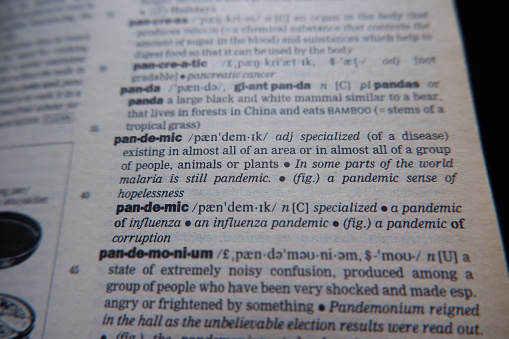 Blurred dictionary page. Close-up to the partial dictionary definition of word pandemic. Selective focus.