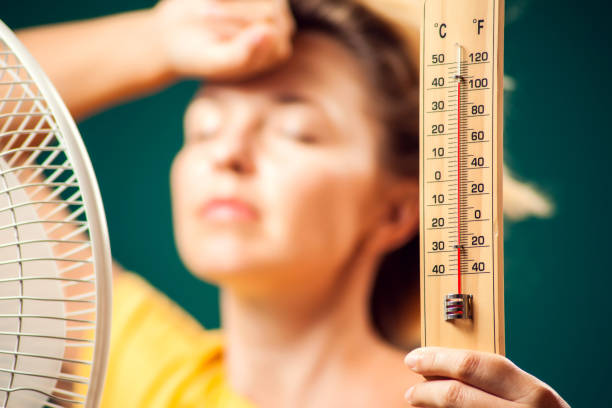 A portrait of woman in front of fan suffering from heat holding thermometer. Close up. Hot weather concept A portrait of woman in front of fan suffering from heat holding thermometer. Hot weather concept heat wave photos stock pictures, royalty-free photos & images