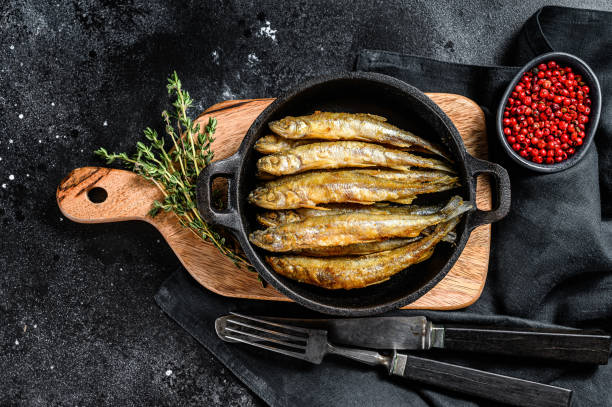 istock Fried smelt in the pan on the table with tomatoes and pepper. Black background. Top view. 1227022903