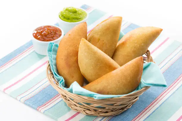 Homemade corn flour empanadas with salsa sauce and guacamole. An empanada is a type of patty baked or fried very popular in many countries of the Americas and in Spain. Empanadas are made by folding dough over a stuffing, which may consist of meat, cheese, fish or other ingredients.