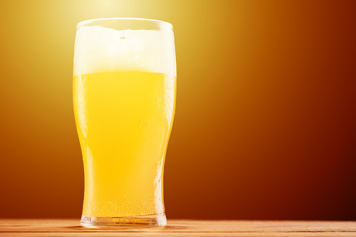 Glass of wheat beer with foam on dark background