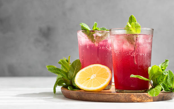 Cold sparkling hibiscus or karkade tea with lemon, mint and ice in glasses on a grey stone background. Summer drink, lemonade. Cold sparkling hibiscus (karkade) tea with lemon, mint and ice in glasses on a grey stone background. carbonated juice stock pictures, royalty-free photos & images