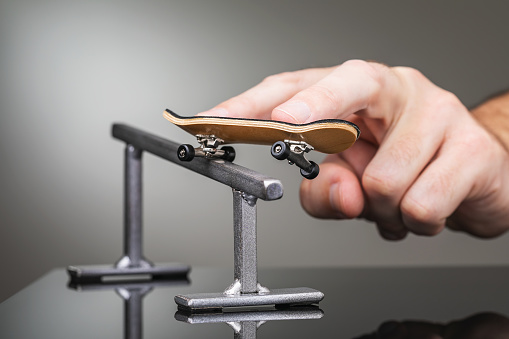 A man rolls a fingerboard on a metal railing, close-up