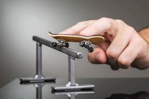 Photo of A man rolls a fingerboard on a metal railing, close-up