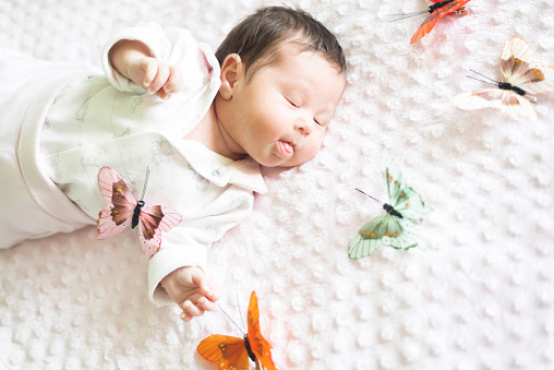 Beautiful two months old newborn is surrounded by colorful toy butterflies