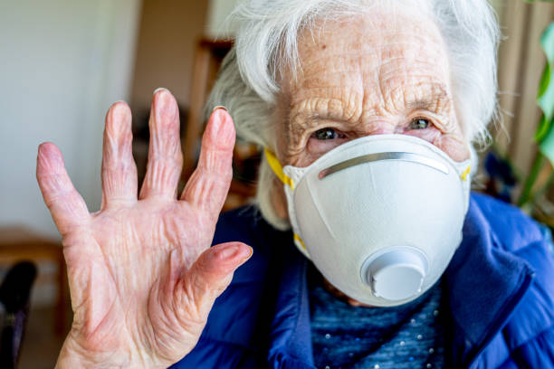 close-up shot of elderly senior caucasian woman smiling holding her hands up waving hello or goodbye wearing an n95 protective face mask to prevent the spread of covid sars ncov 19 coronavirus swine flu h7n9 influenza illness during cold and flu season - flu virus cold and flu swine flu epidemic imagens e fotografias de stock