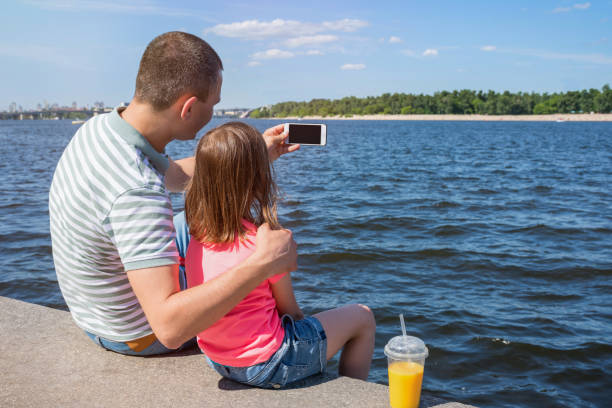 ojciec i dziecko robią sobie selfie nad rzeką w słoneczny dzień. widok z tyłu. zbliżenie. styl życia. - sunny cheerful close up outdoors zdjęcia i obrazy z banku zdjęć