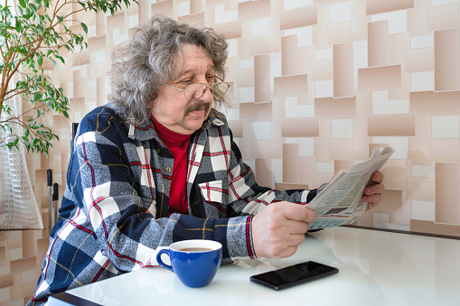 A portrait of a 60-year old man reading news. A newspaper in a pensioner's hands.