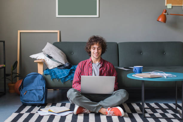 lächelnder college-student sitzt auf dem boden und benutzt seinen laptop - student teenager adolescence teenagers only stock-fotos und bilder