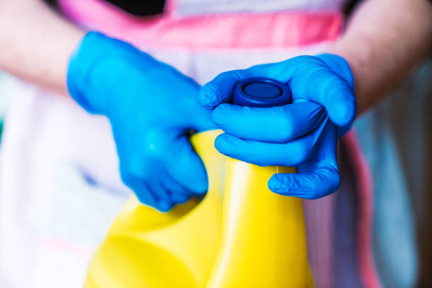 Housewife with blue latex gloves and apron opening a yellow bottle of bleach. Housewife with blue latex gloves and apron opening a yellow bottle of bleach. bleach stock pictures, royalty-free photos & images