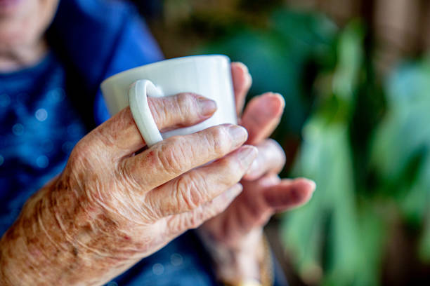 Close-Up Shot of Elderly Senior Caucasian Person's Hands Holding a Coffee or Tea in a White Ceramic Mug Indoors Looking Out the Window in the Summer Close-Up Shot of Elderly Senior Caucasian Woman's Hands Holding a Coffee or Tea Drink Beverage in a White Ceramic Mug Indoors Looking Out the Window in the Summer cup of tea hands stock pictures, royalty-free photos & images