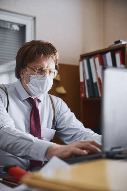 istock Aged manager sitting by his computer in disposable medical mask on face 1227036267
